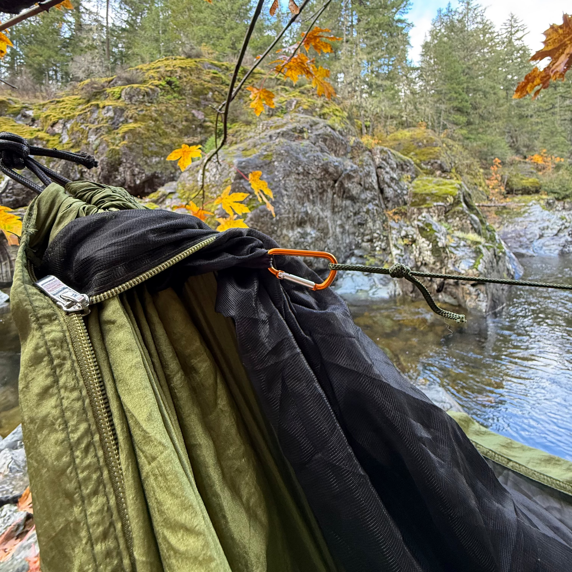 Insulated Hammock hanging from a tree branch with a scenic background of water and trees.
